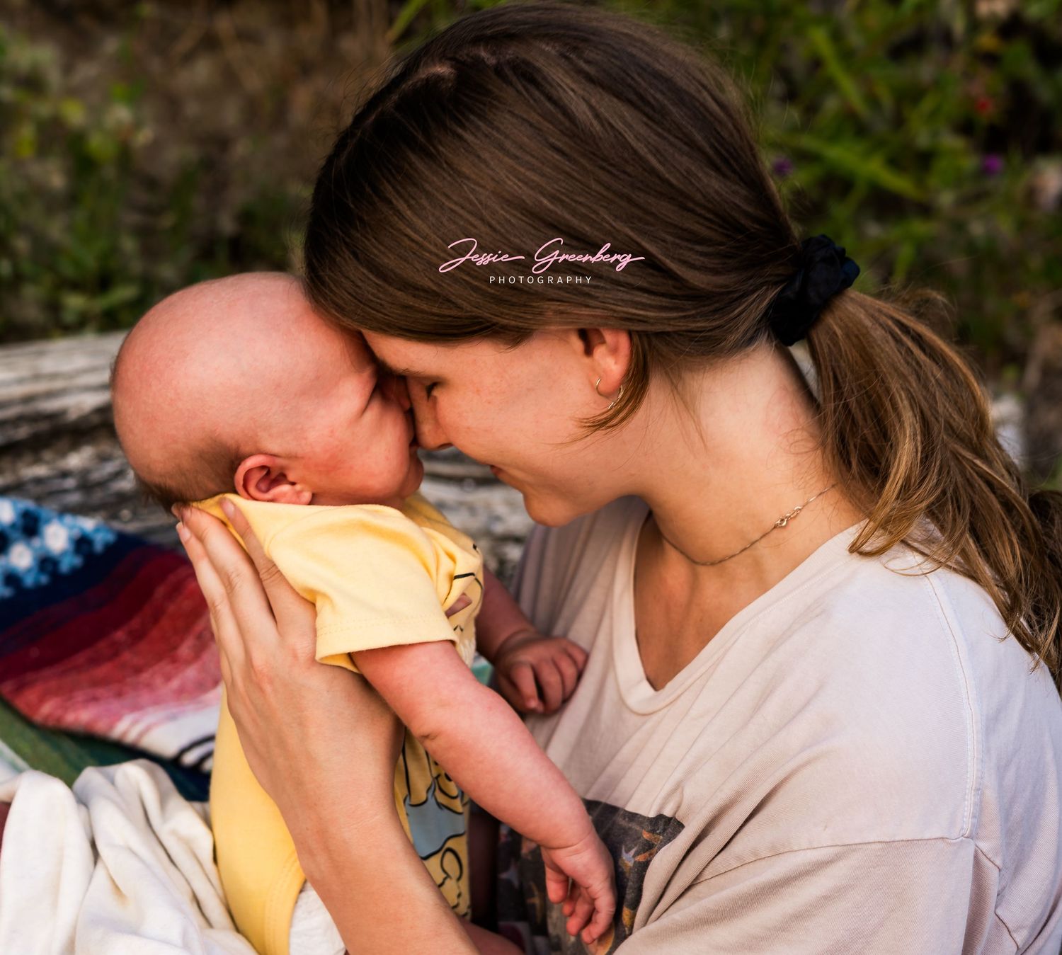 A mother tenderly touches foreheads with her newborn baby, sharing an intimate bonding moment outdoors.