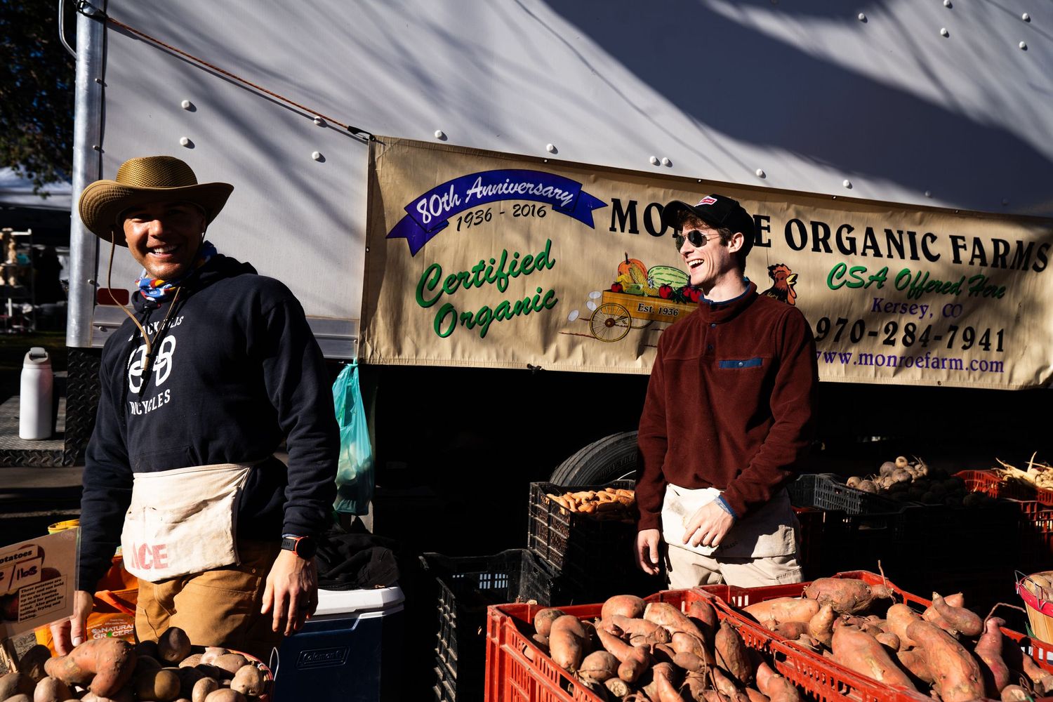 Bustling farmers market with vendors selling fresh produce under white canopy tents.
