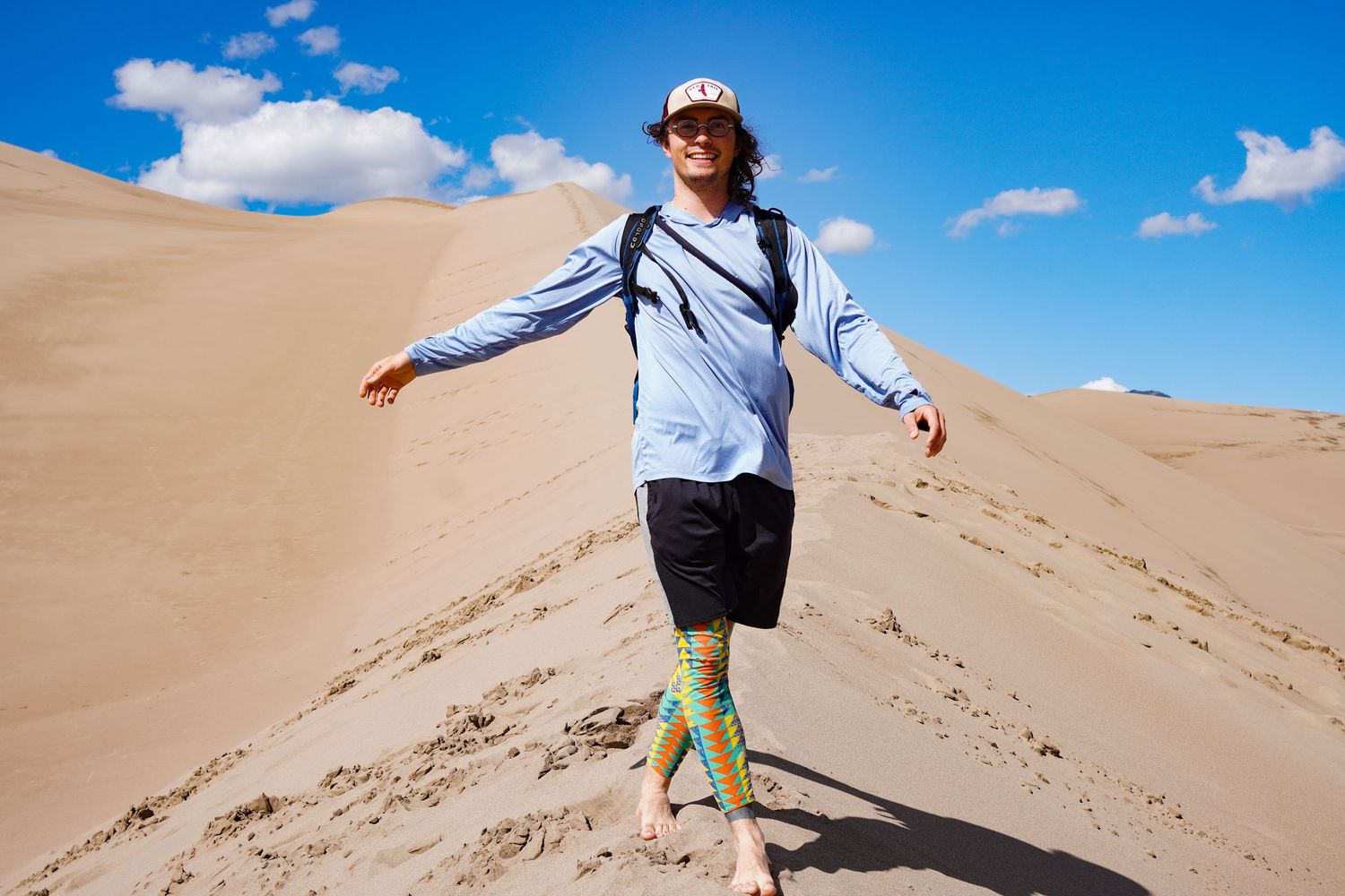 Person sandboarding down massive sand dune under bright blue sky.