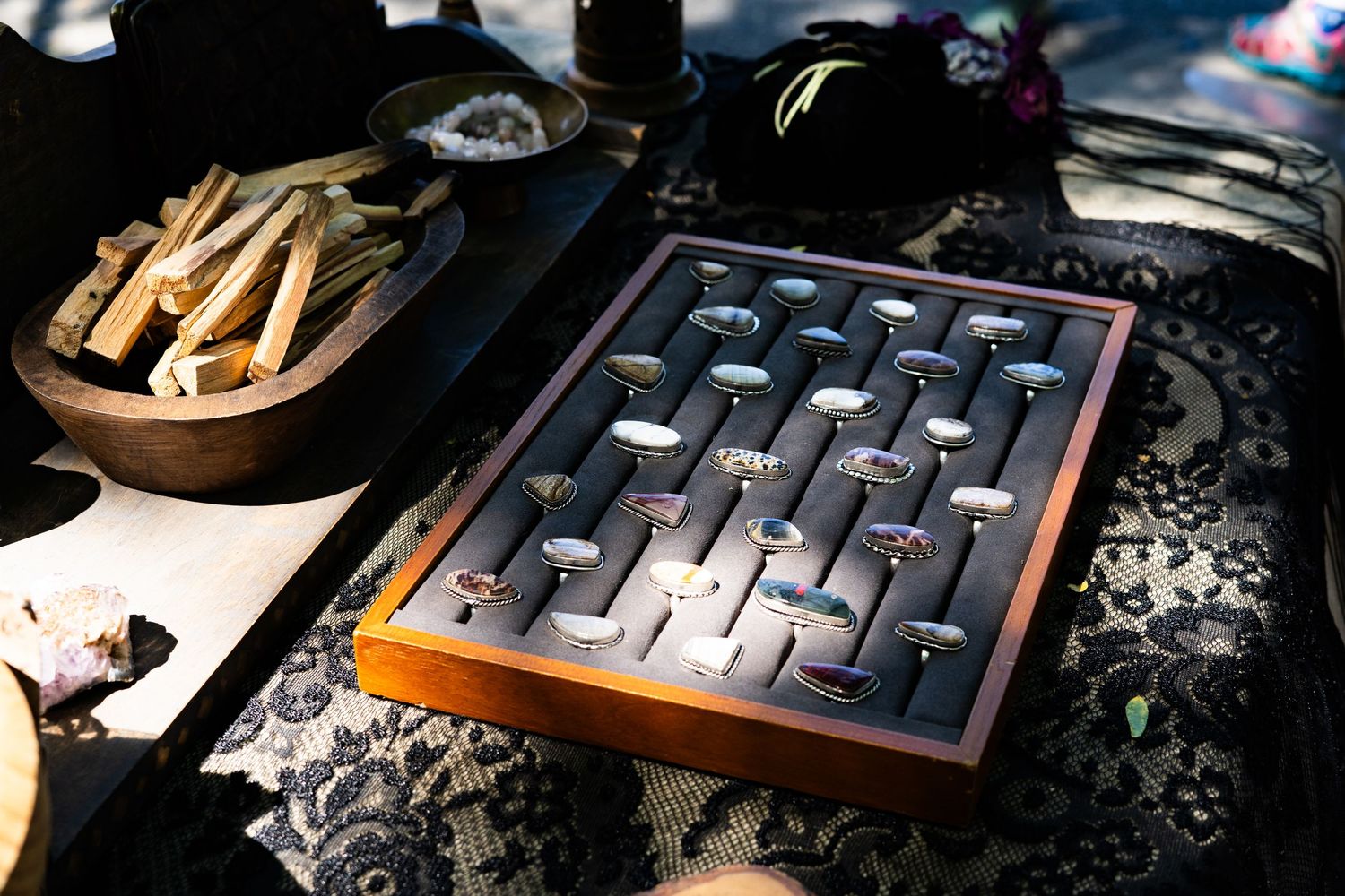 A wooden display tray showcasing silver rings on gray velvet at an outdoor jewelry market booth.