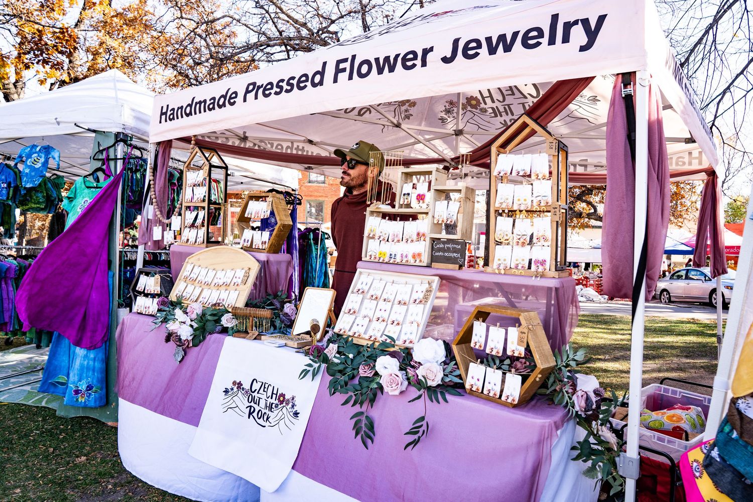 Man wearing a hat and sunglasses at the Hand Pressed Flower Jewelry booth at the farmers market.