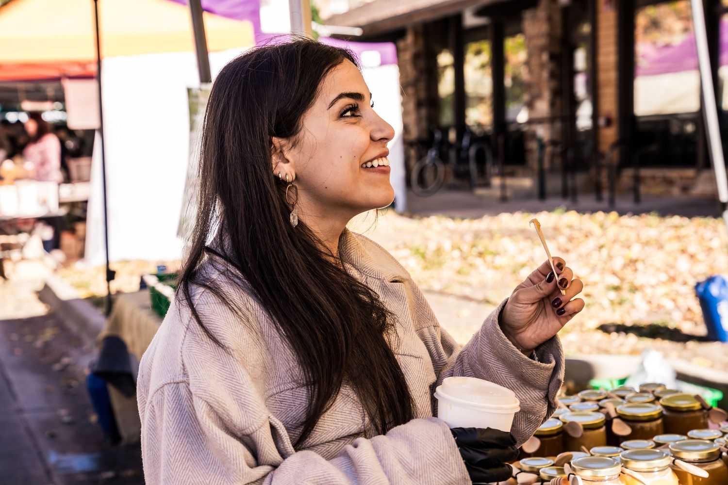 Young girl with black hair excitedly tasting local honey at Boulder Farmers Market, enjoying Colorado-made Happy Bees honey.