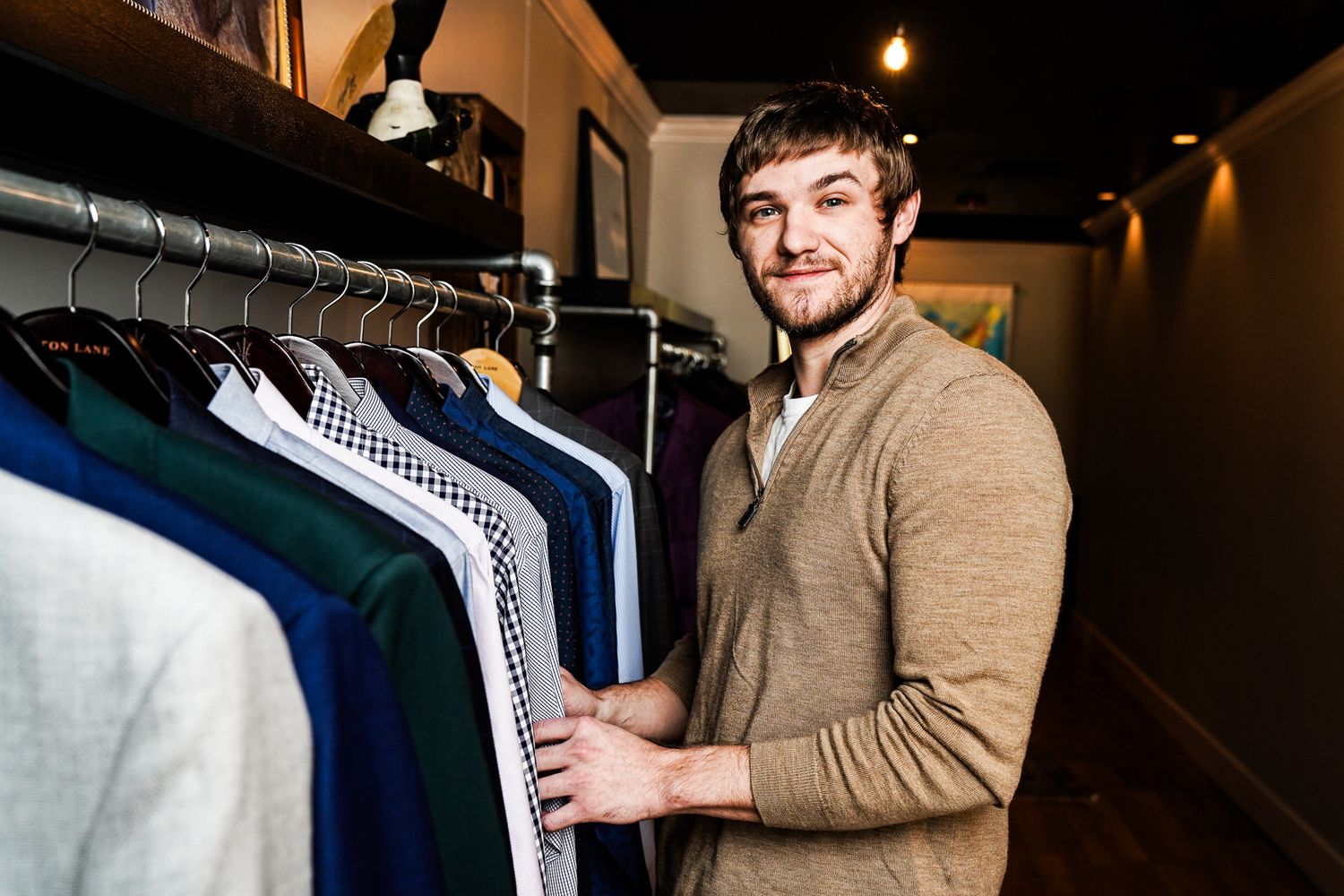 A person in a tan sweater browses through clothing racks in a retail store.