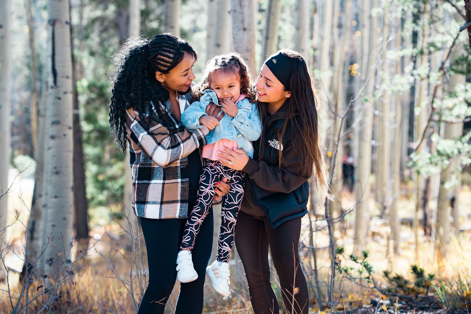 A family enjoys a tender moment together in a serene forest setting with tall trees in the background.