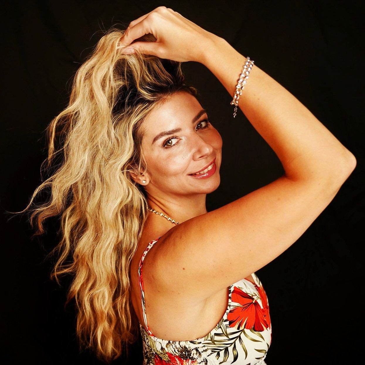 a blonde woman wearing a red flower dress against a black backdrop.