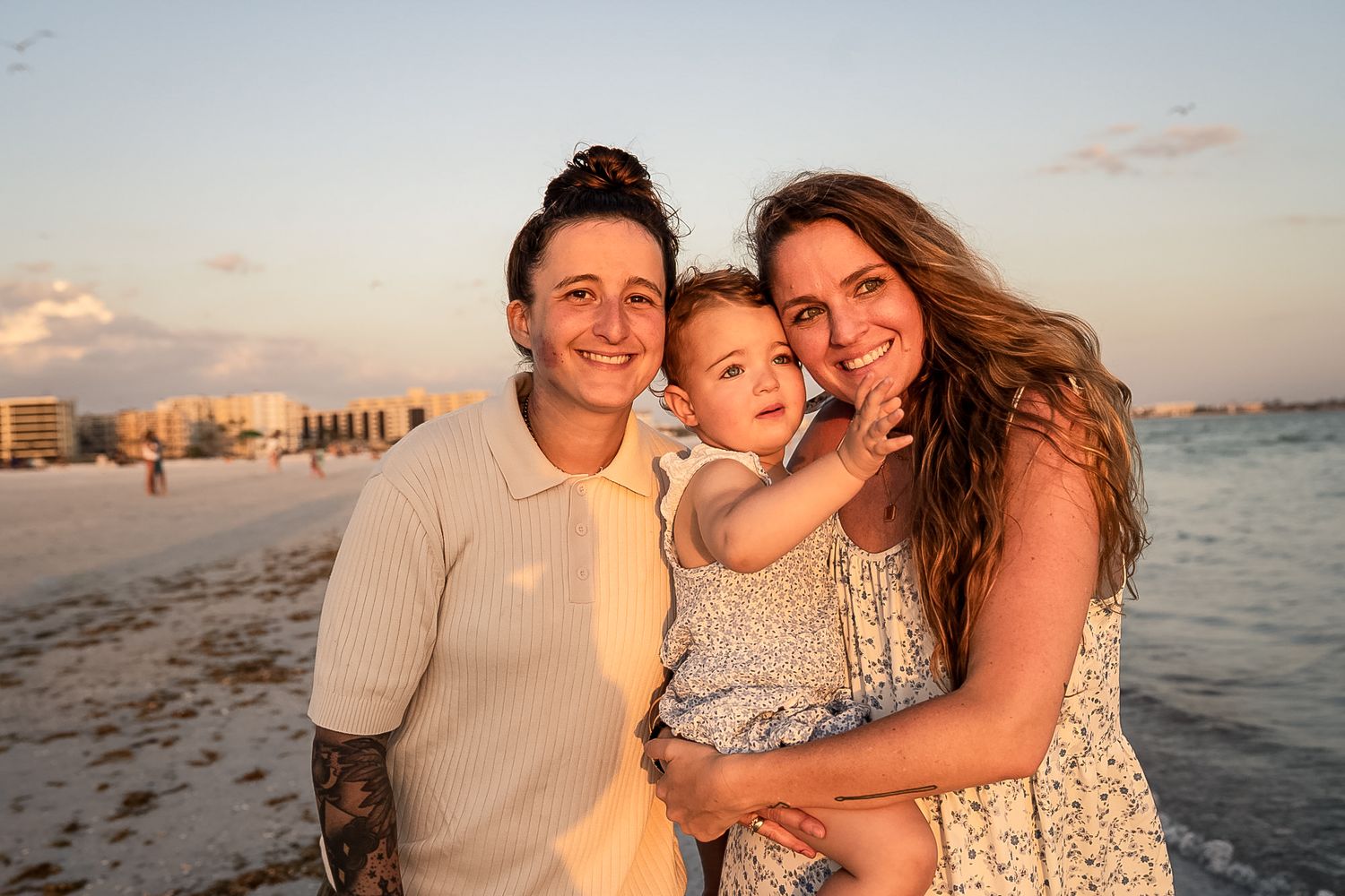 A photo of the two wives with their baby girl and a sunset on the beach.