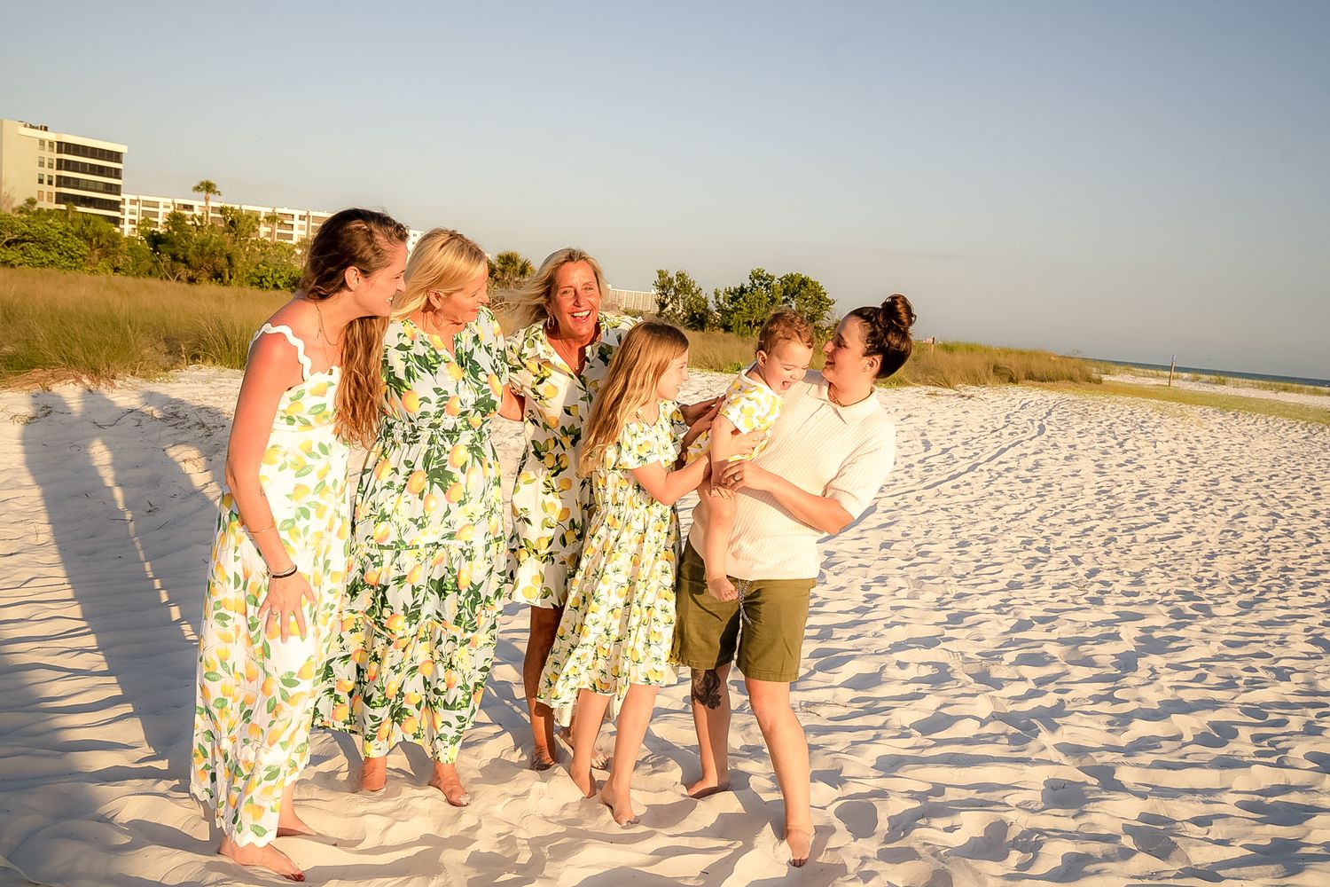 A photo of all women smiling at each other on the beach with the blue sky behind them.