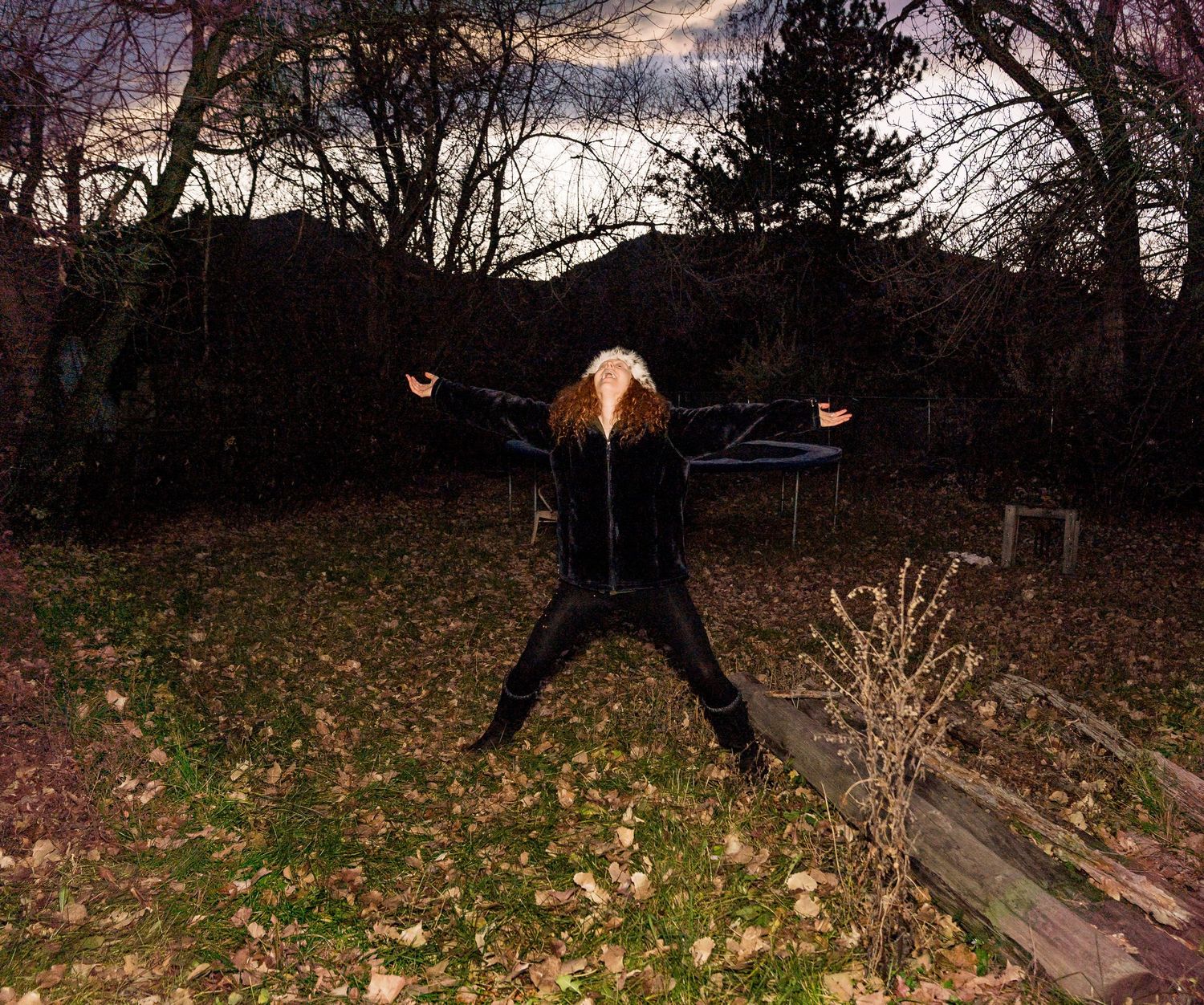 A person performs a sequence of acrobatic flips and movements on a backyard trampoline at dusk.