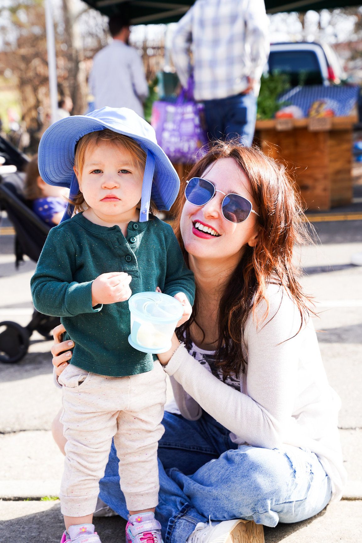A woman smiles as she holds her baby boy wearing a bright blue hat while they enjoy live music in downtown Boulder.