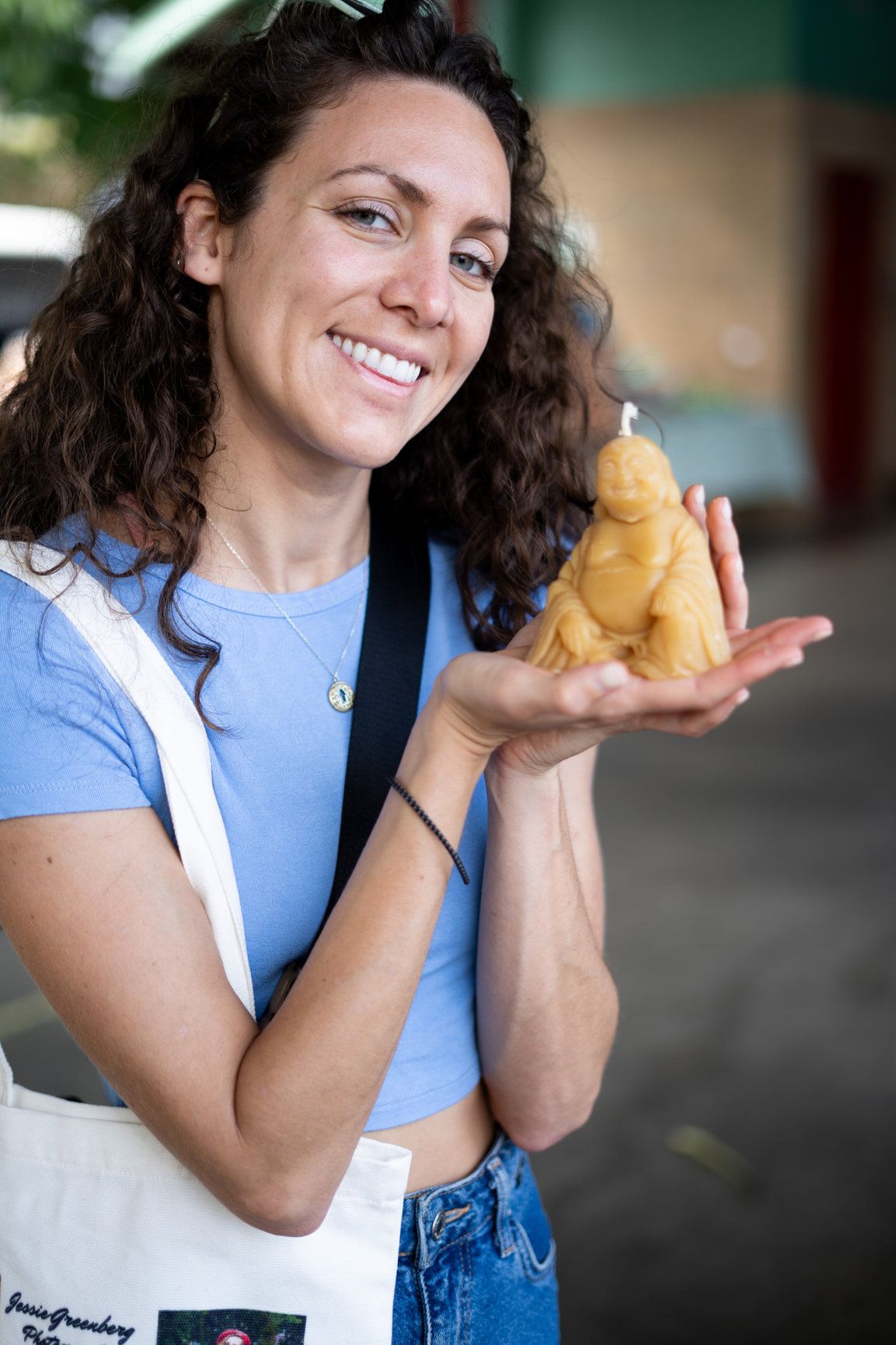 A photo of a woman with brown wavy hair holding a beautiful Buddha-shaped candle, she is smiling brightly.