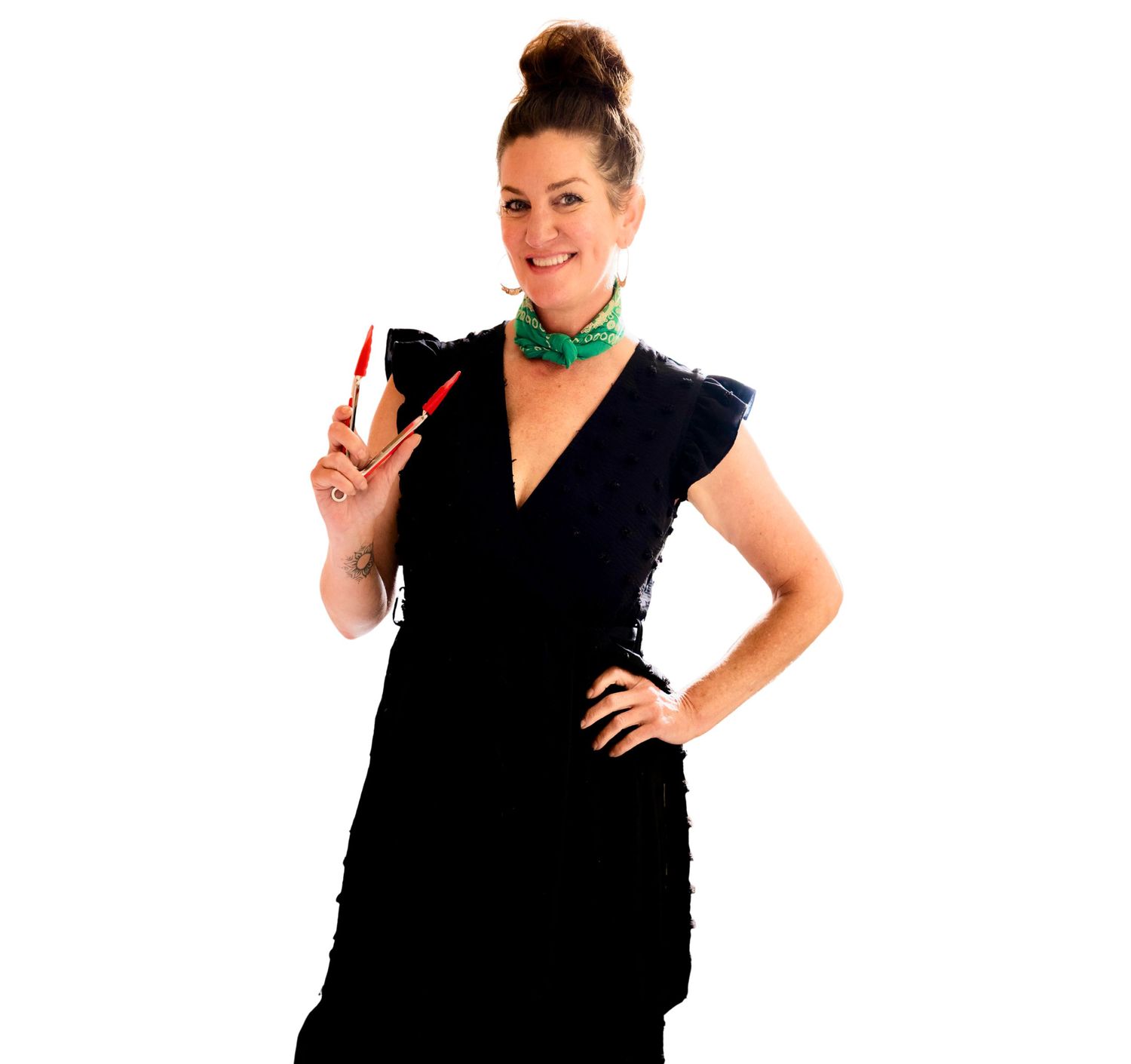 Woman in black dress holding a red pen, wearing green necklace, posing confidently on white background.