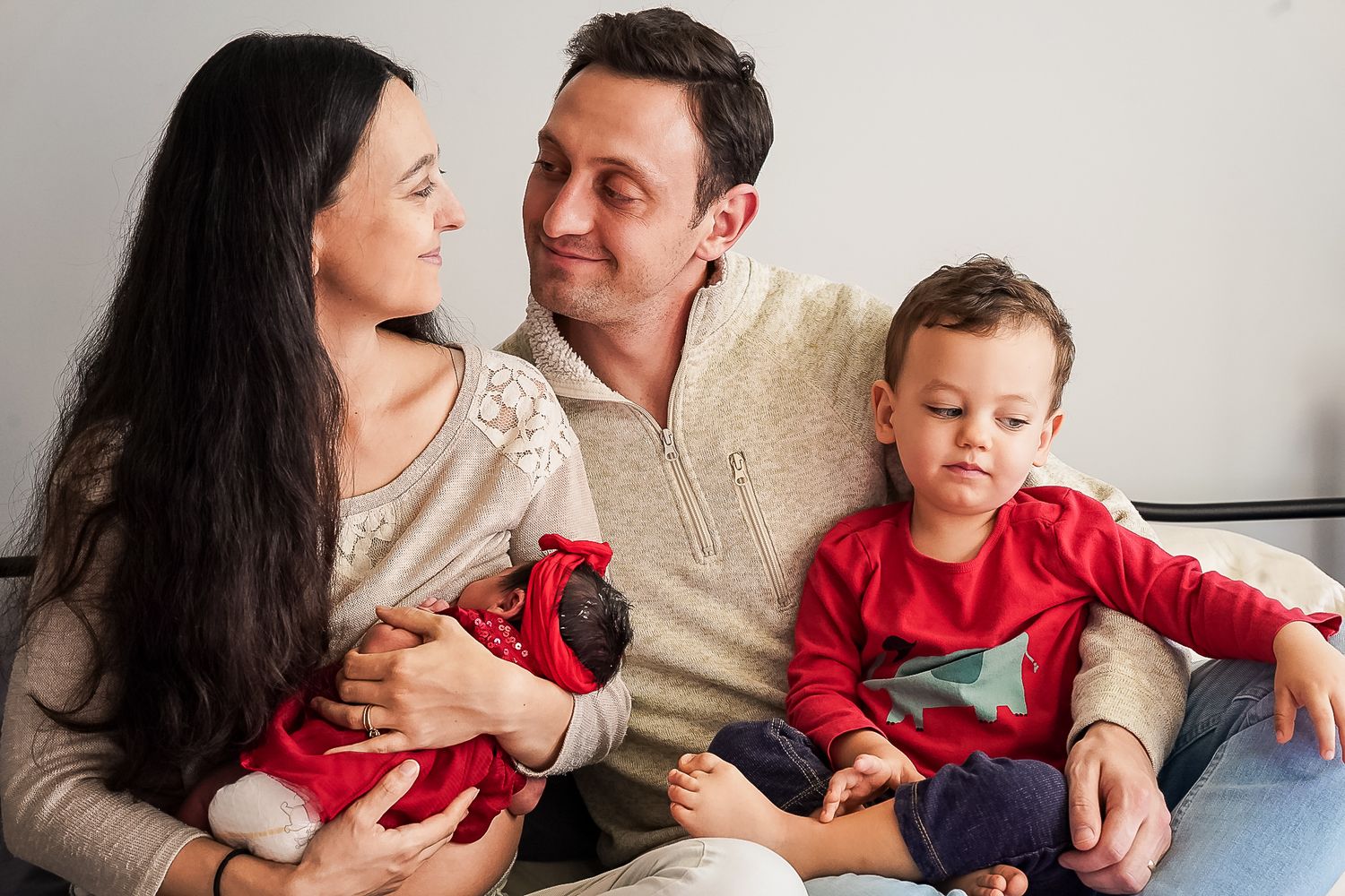 Happy family with parents and two young children sitting together on a couch, smiling warmly at each other.