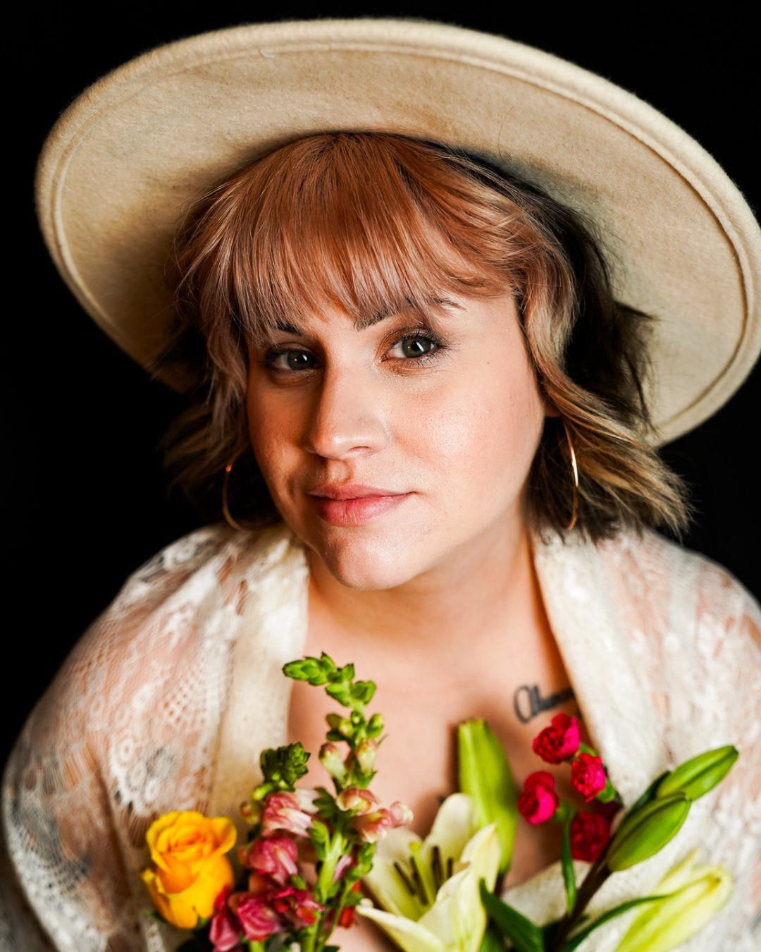 Woman in lace top and tan hat holding colorful bouquet.