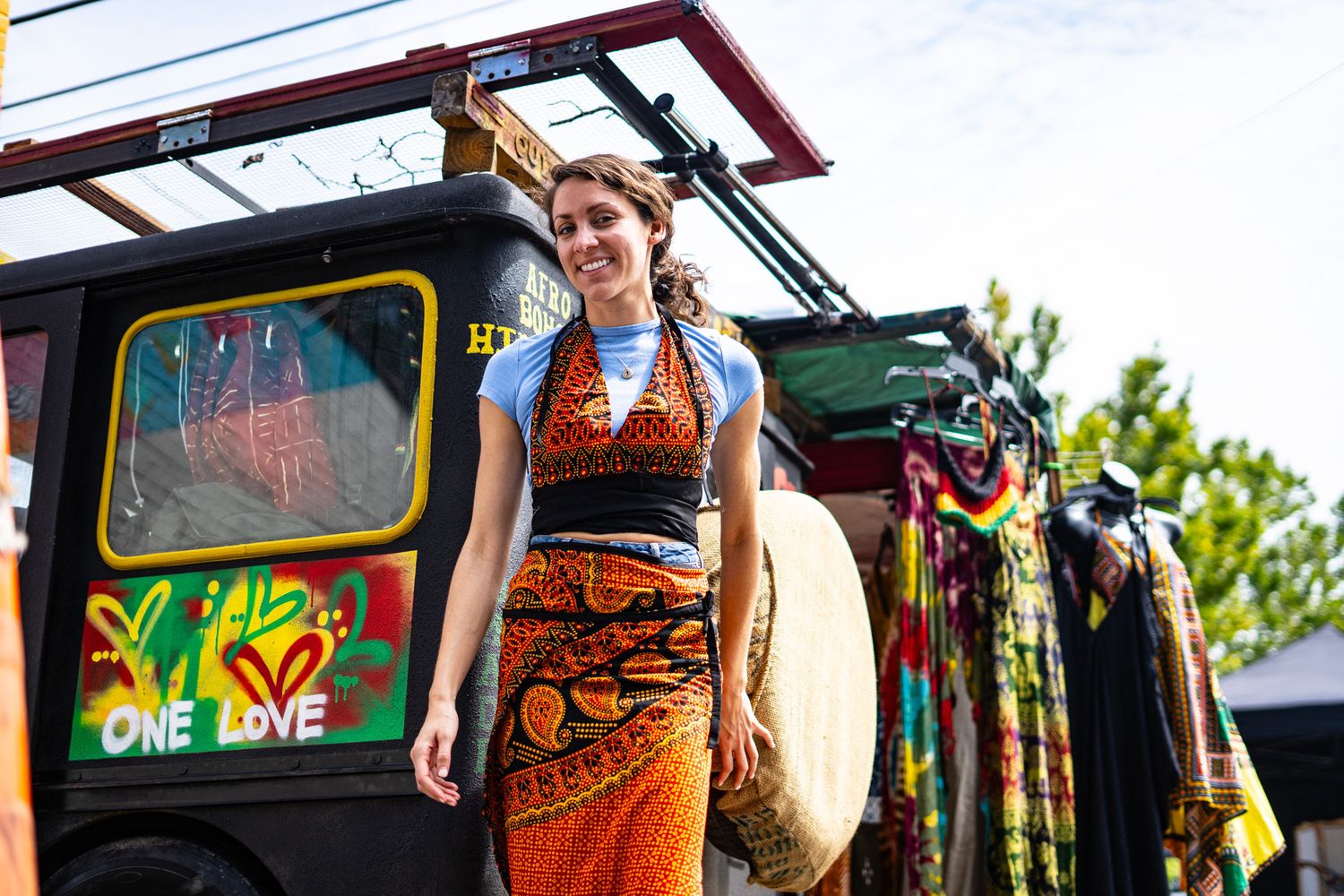 A photo of a brown haired girl smiling in her dress outside of a clothing store with a patterned dress.