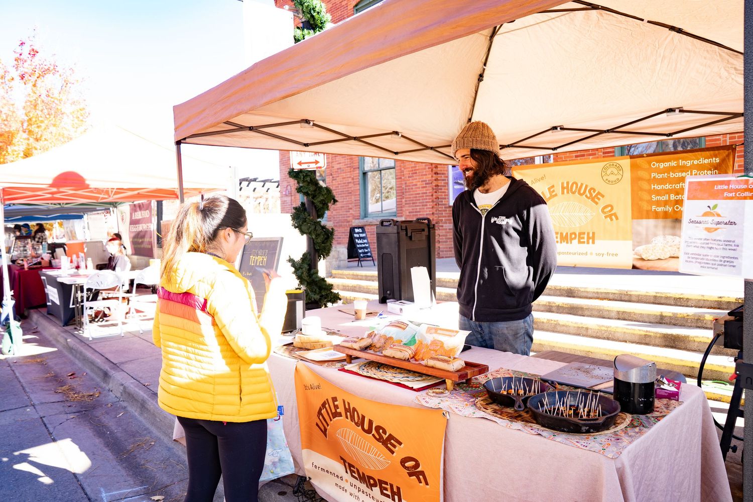 Man smiling and handing out samples at The Little House of Tempeh booth at the farmers market.