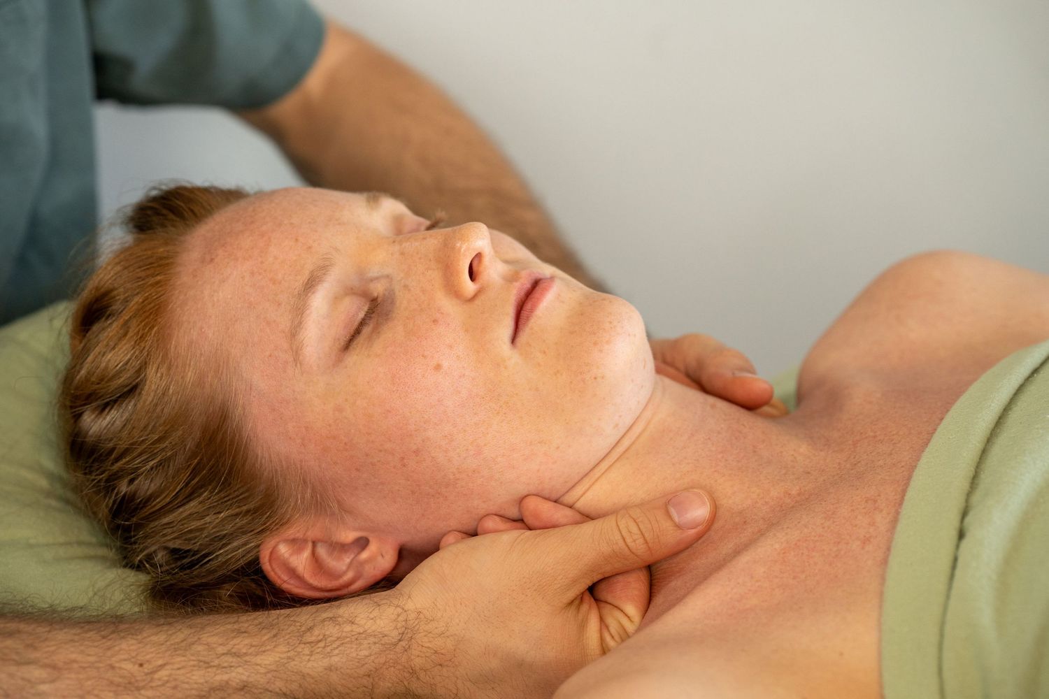 Therapist performing a gentle neck and shoulder massage on a relaxed woman lying on a massage table.