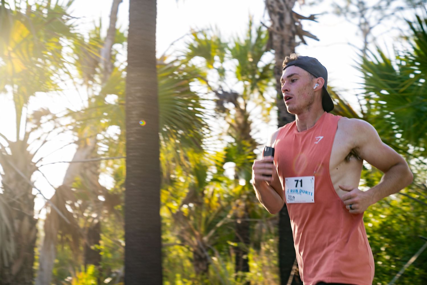A man running outdoors wearing a peach tank top, showcasing muscular arms.