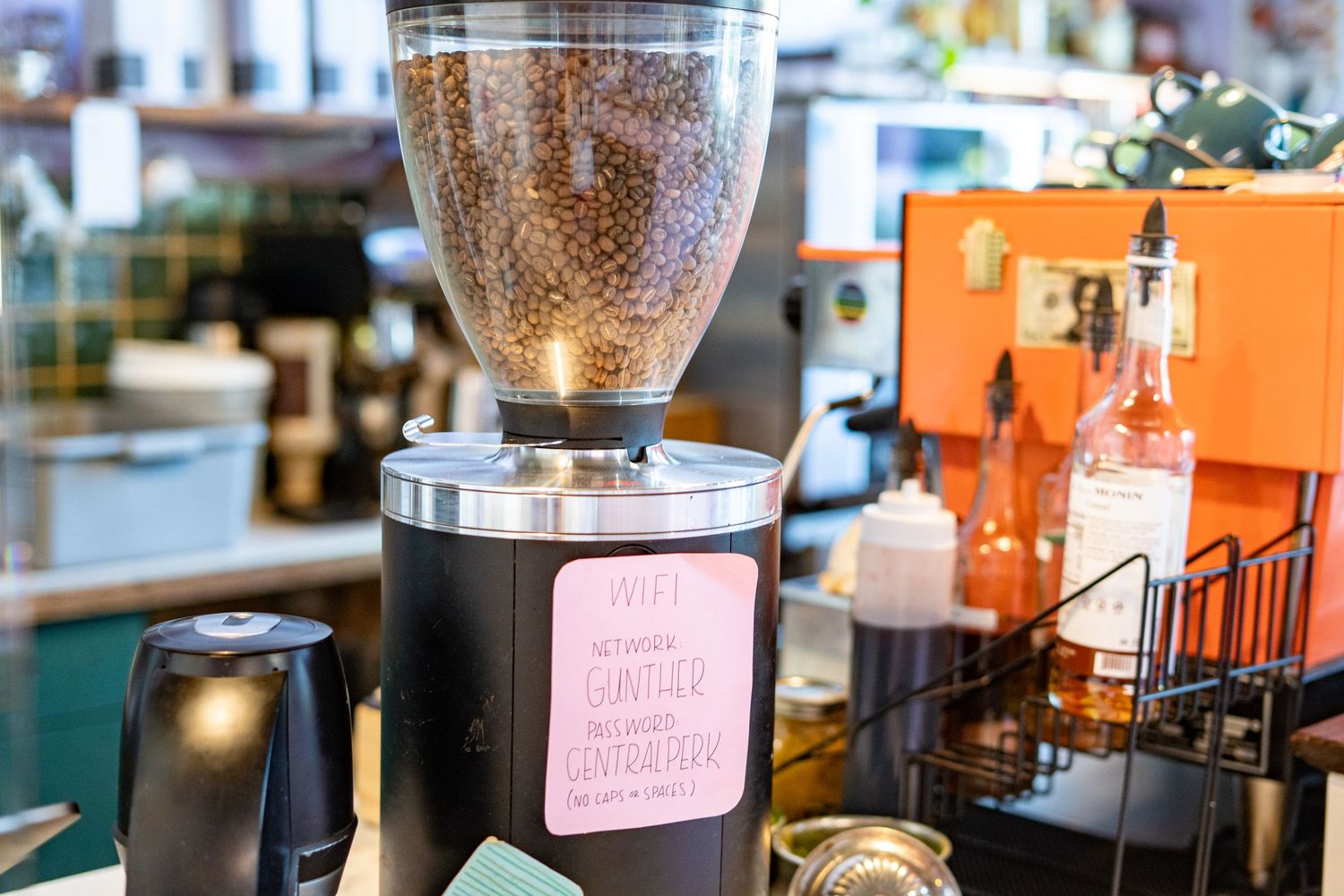 Close-up of a commercial coffee grinder filled with roasted beans on a cafe counter with equipment in background.