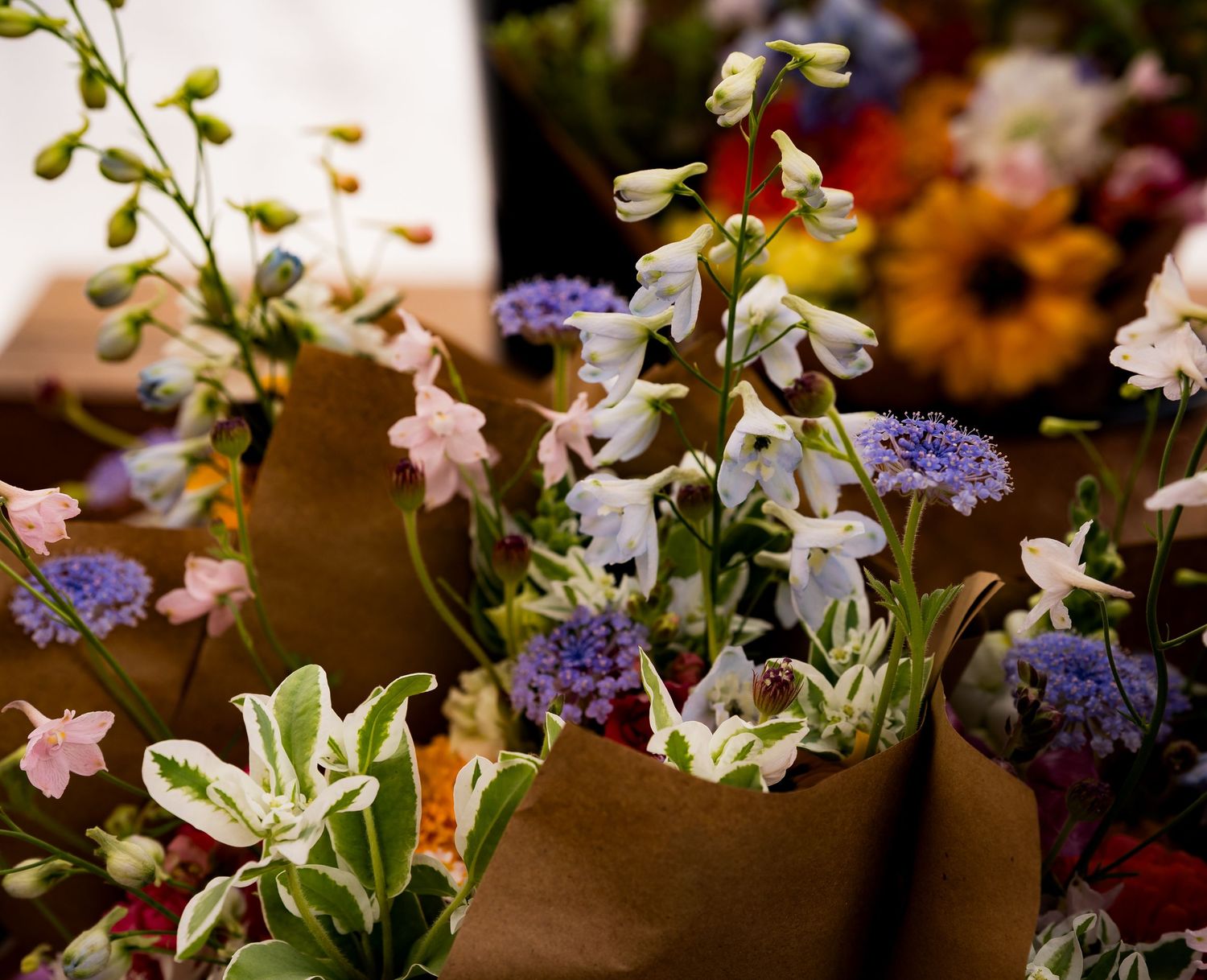 Colorful wildflower bouquets wrapped in brown kraft paper displayed at a flower market stall.