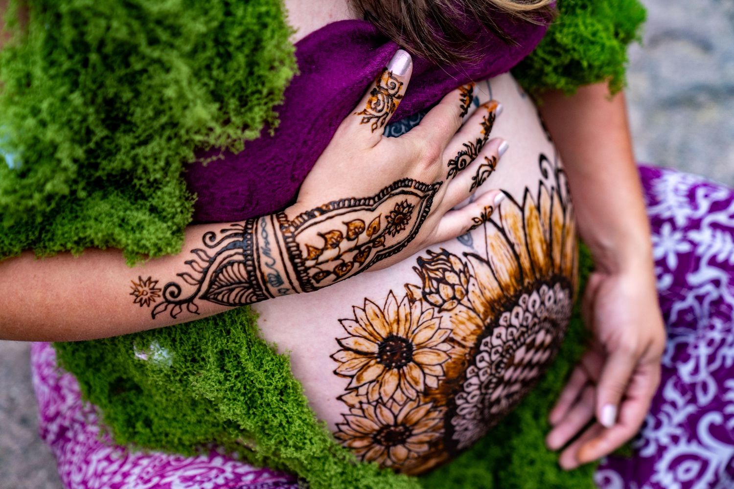Intricate floral henna designs adorning hands against a backdrop of vibrant green moss and purple flowers.