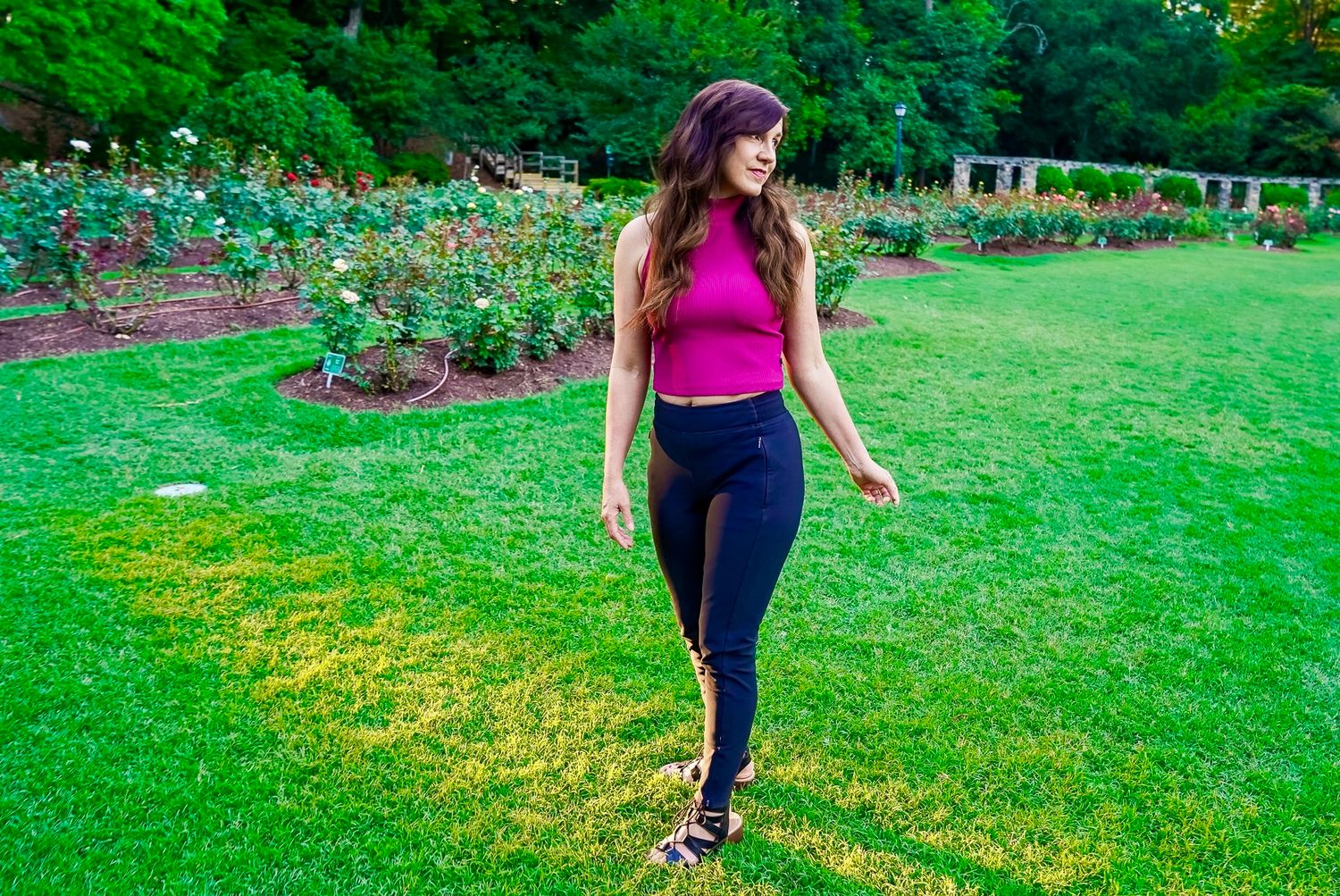 Person in pink top and black pants walking through a vibrant green garden with yellow wildflowers.