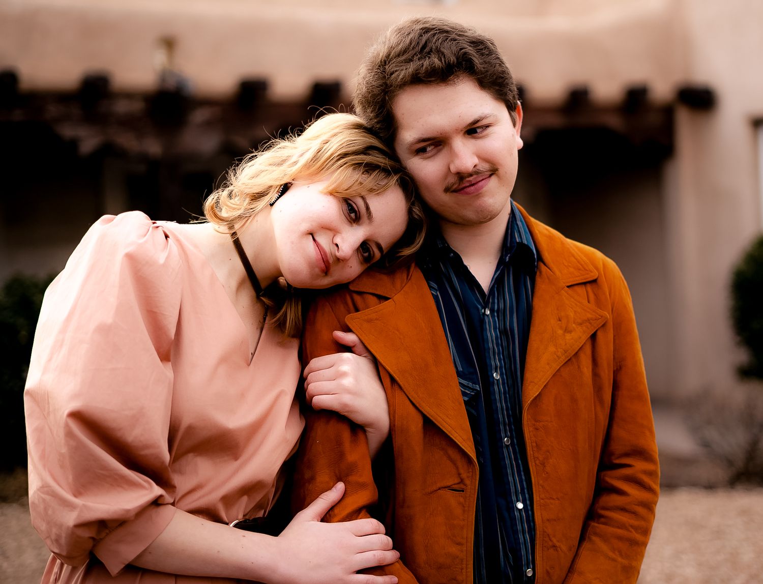 A couple in brown and pink coats share intimate moments in a series of outdoor portrait photographs.