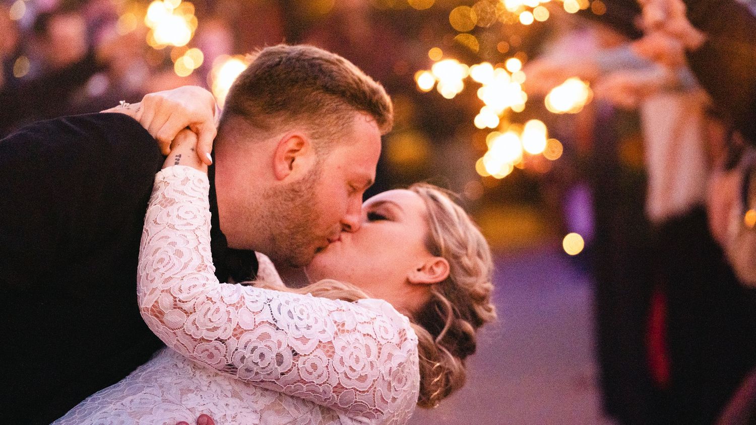 A couple shares a romantic kiss at their wedding reception with sparkling bokeh lights glowing in the background.
