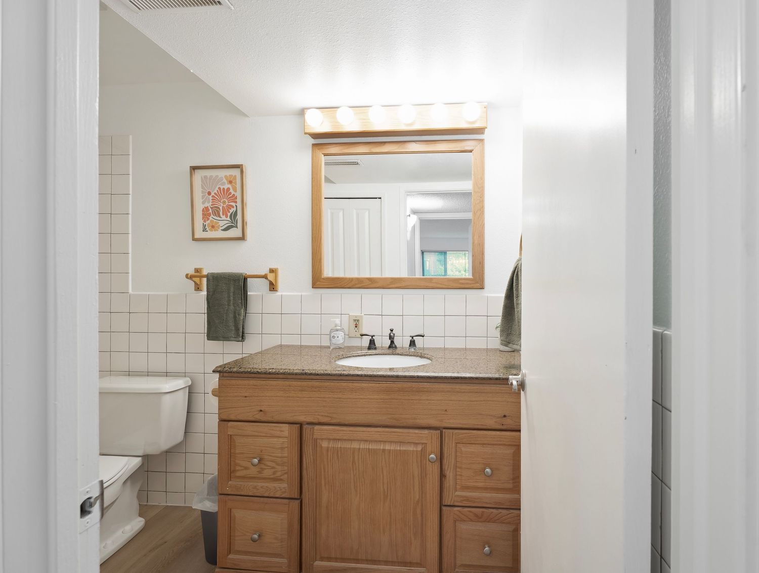 Bathroom with wooden vanity, white tile backsplash, framed mirror, and toilet visible in background.