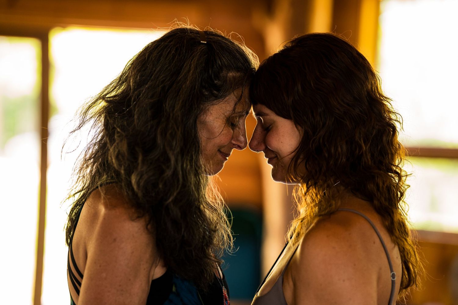 A couple shares an intimate kiss while standing in a warmly lit room with golden ambient lighting.