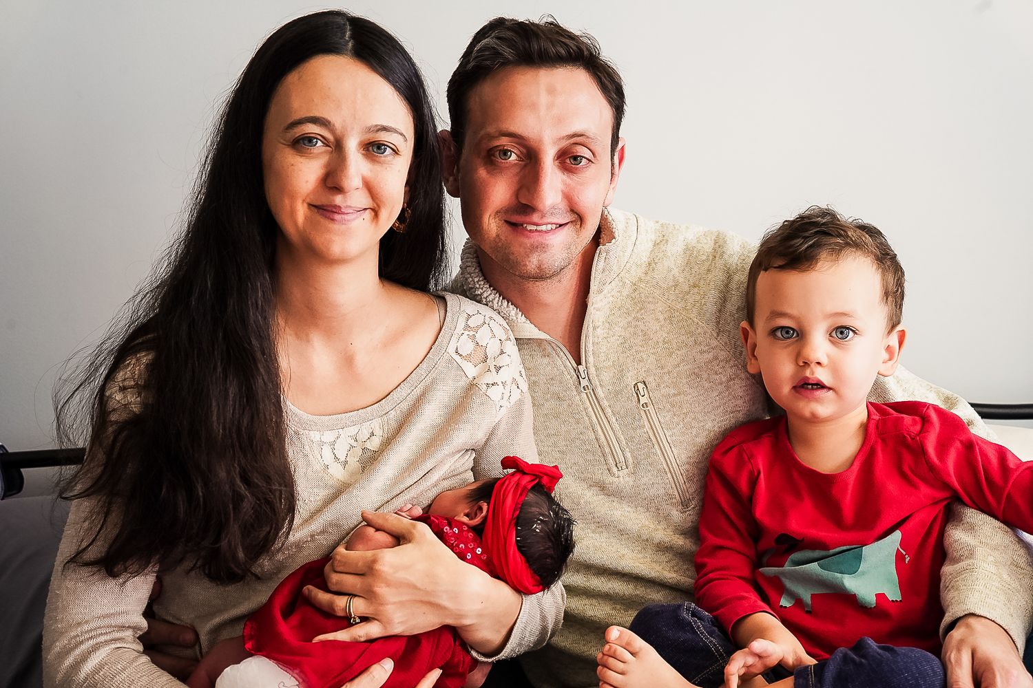 Happy family portrait with parents and two young children sitting together indoors.