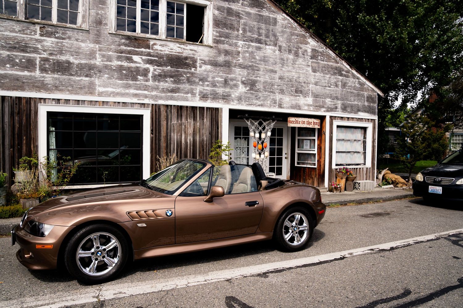 Bronze BMW Z3 convertible parked outside a rustic wooden garage building on a quiet street.