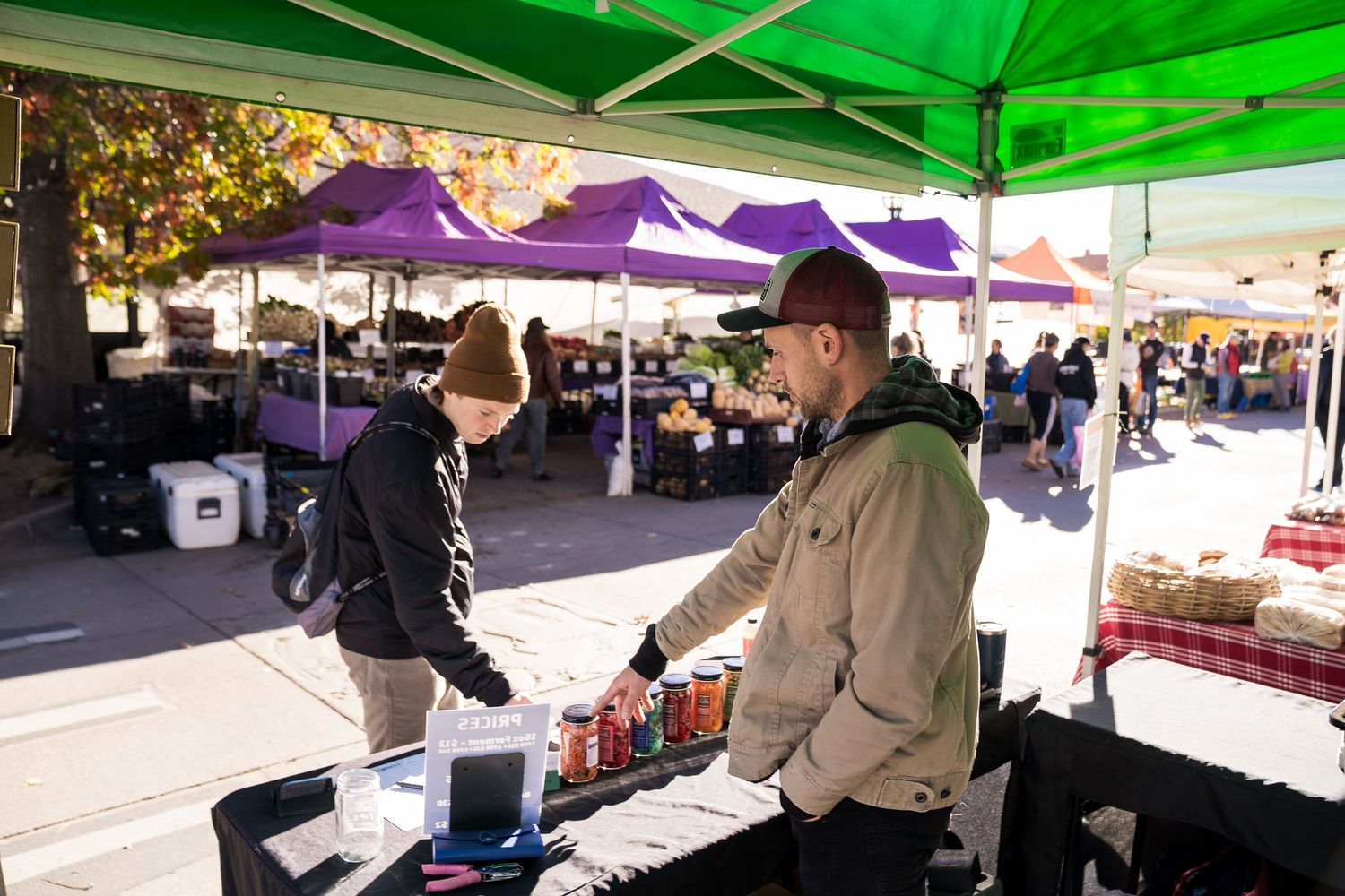 Ferment Culture owner showing a customer colorful jars of fermented foods at Boulder Farmers Market, locally made kimchi and sauerkraut.