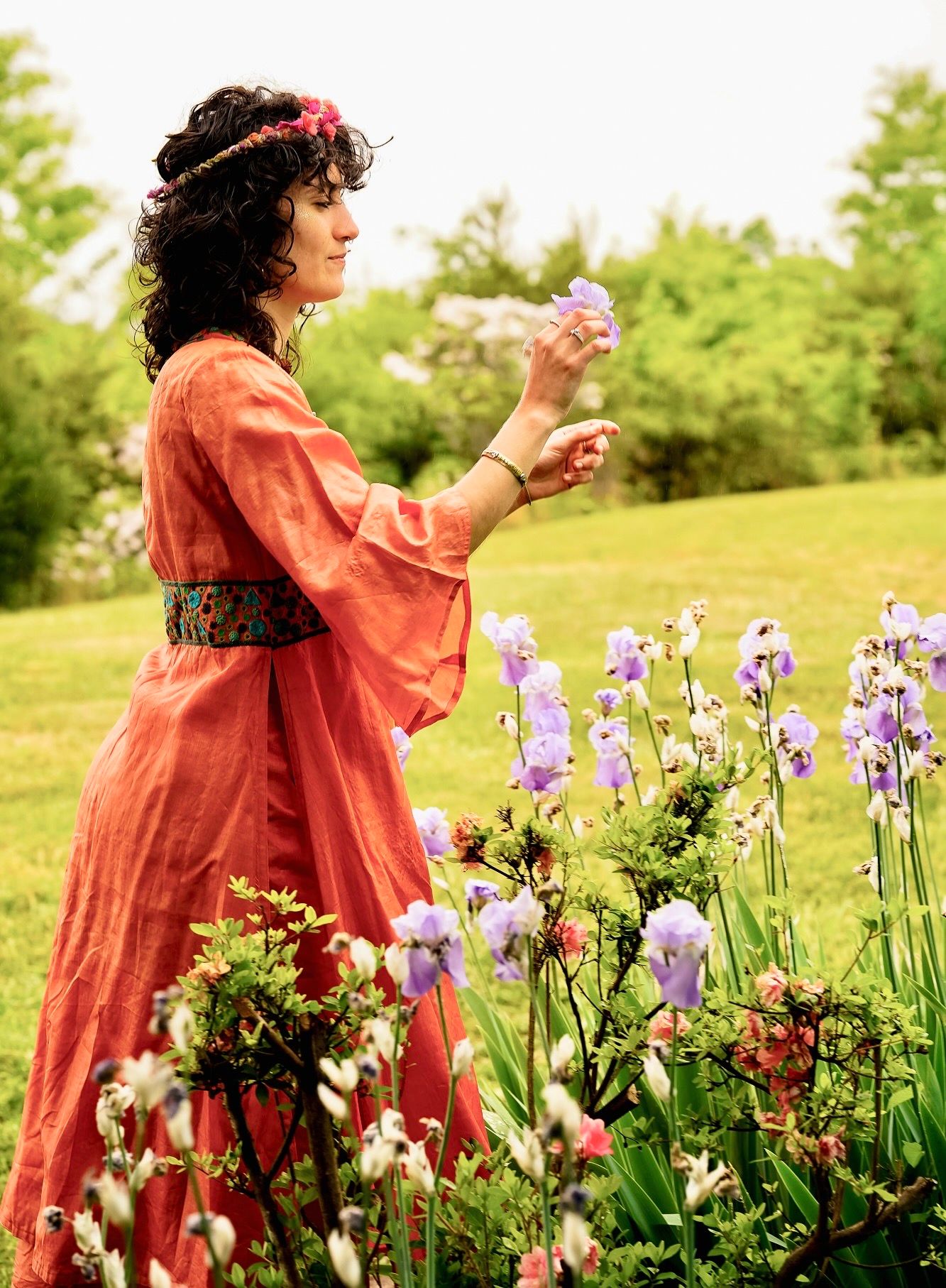 Woman in red dress holding purple flower in lush garden with iris blooms.