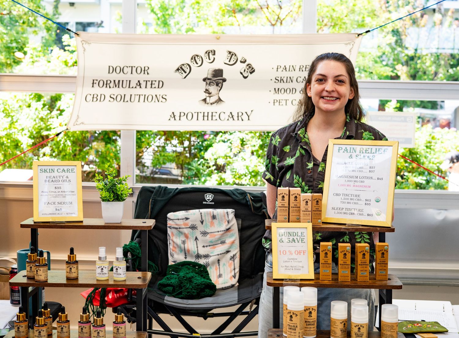Woman smiling at Doc D's Apothecary CBD solutions booth with products displayed on table.