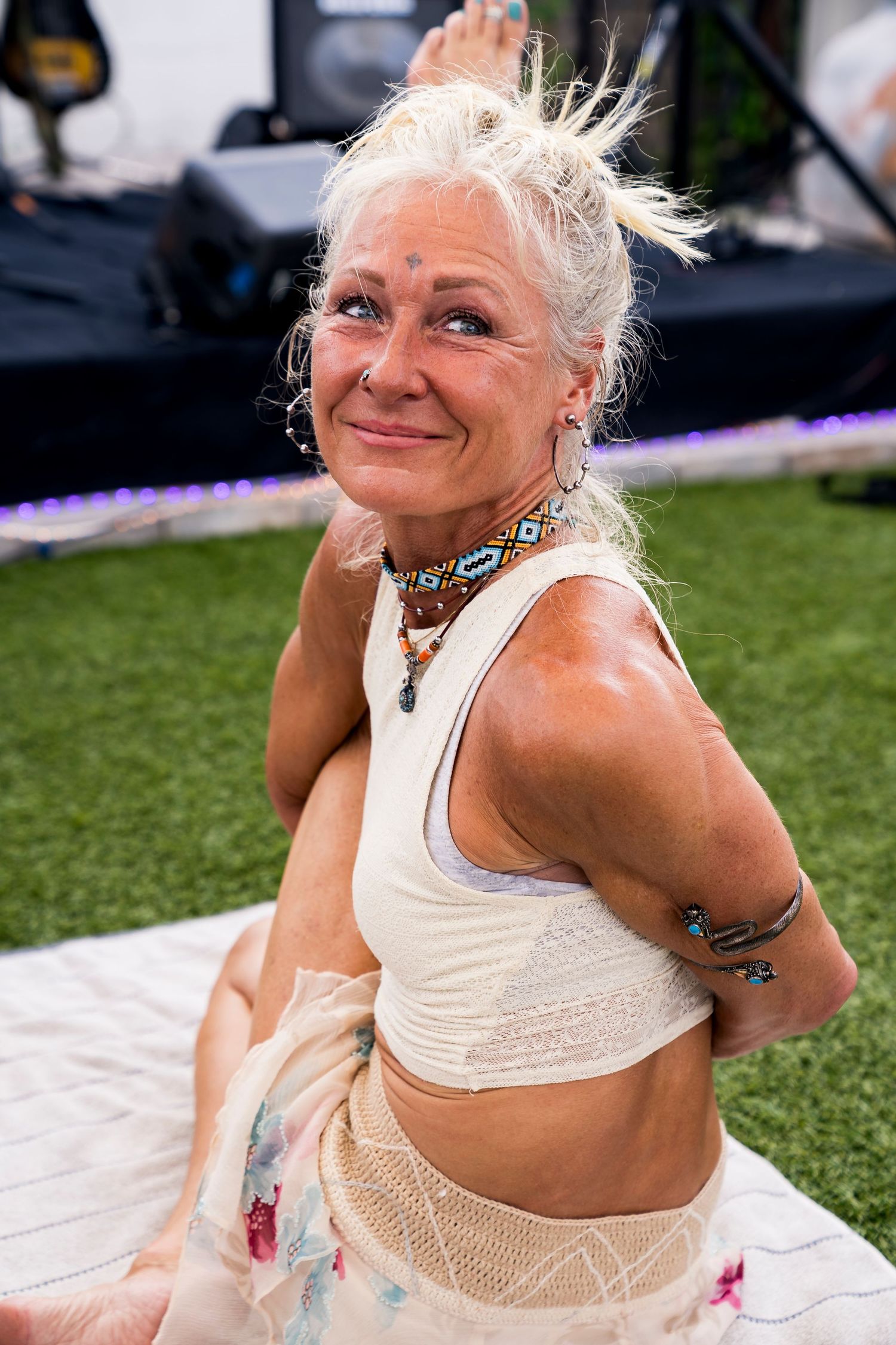 A photo of a woman with a white tank top looking up with white hair and tan shorts.