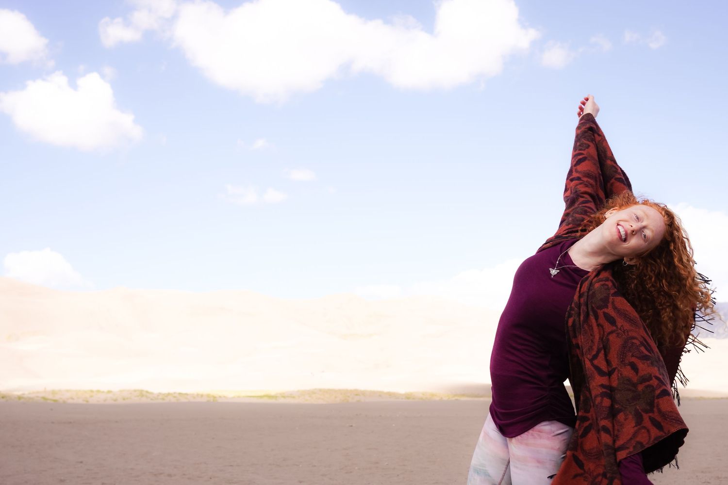 Woman in burgundy sweater dances gracefully against cloudy sky backdrop.