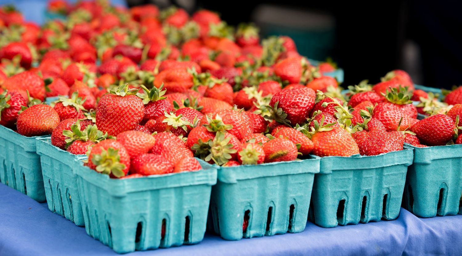 Fresh red strawberries in green cardboard pint containers displayed at an outdoor farmers market.