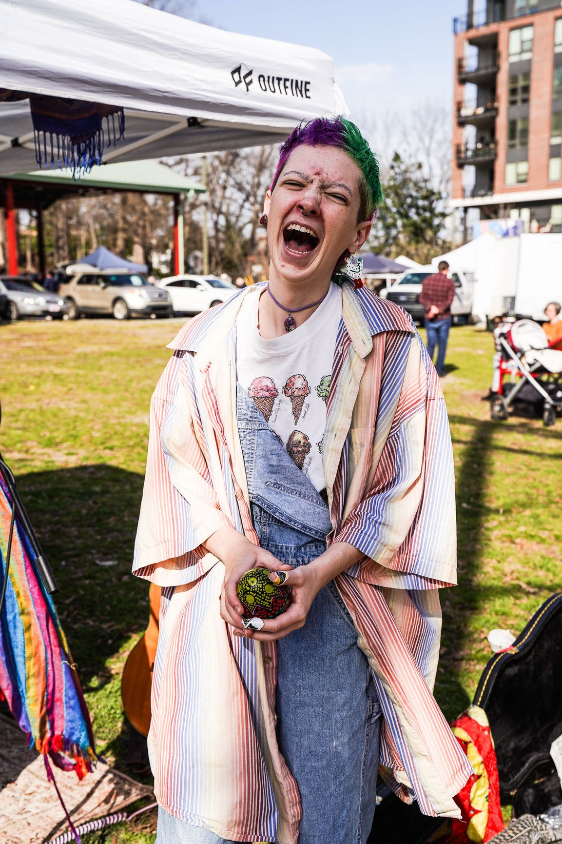 A woman with colorful hair laughs joyfully while holding a maraca during a lively moment in downtown Boulder.