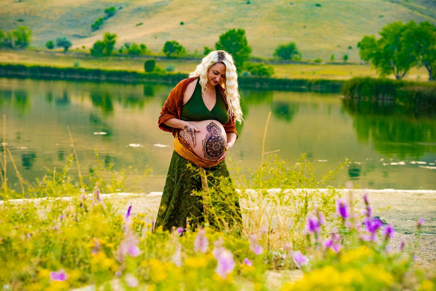 A person in a black dress walks through a vibrant meadow of wildflowers beside a tranquil lake on a sunny day.