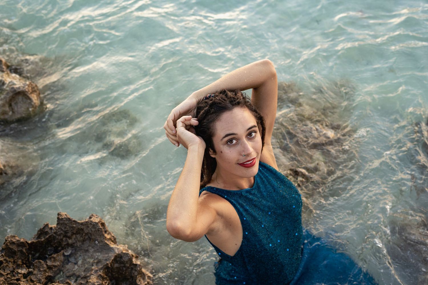 A person in a dark blue dress poses gracefully in crystal clear turquoise ocean water.