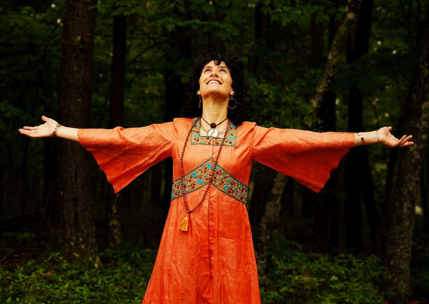a photo of a woman wearing a beautiful orange dress with hands out to the side, she is looking up and smiling.