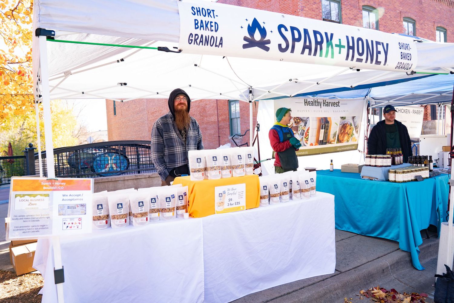 Man with an orange beard smiling at the Spark and Honey booth at the farmers market.