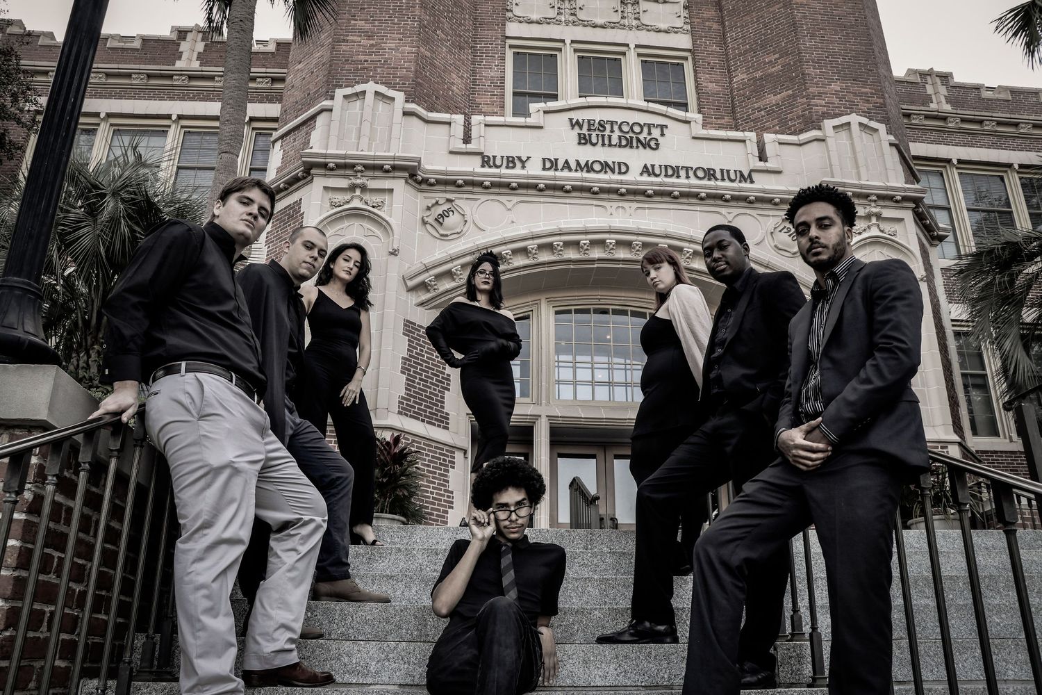 A music group poses dramatically on steps outside Ruby Diamond Auditorium in formal attire.