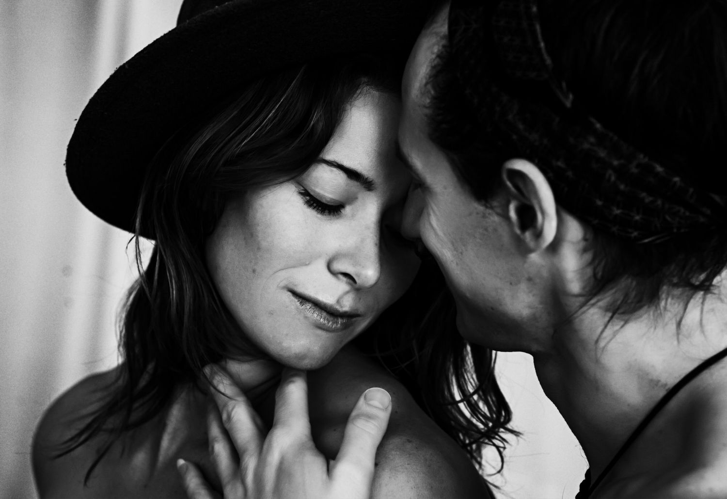 Black and white photo of two people in an intimate moment, woman wearing a hat with eyes closed.