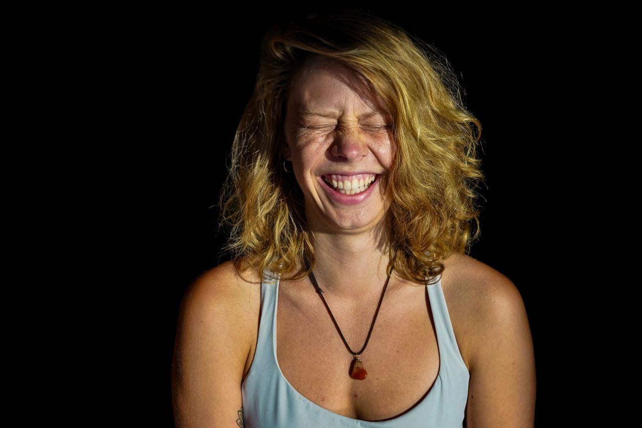 Laughing redhead woman in blue tank top against black background.