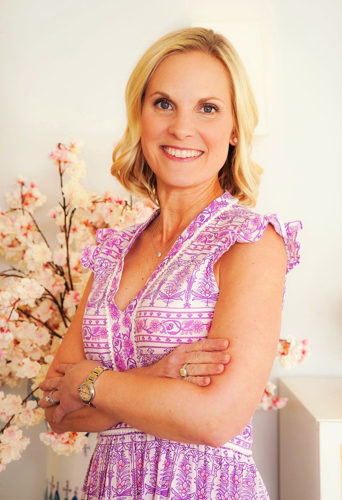 A photo of a blonde woman with her arms crossed wearing a beautiful pink dress.