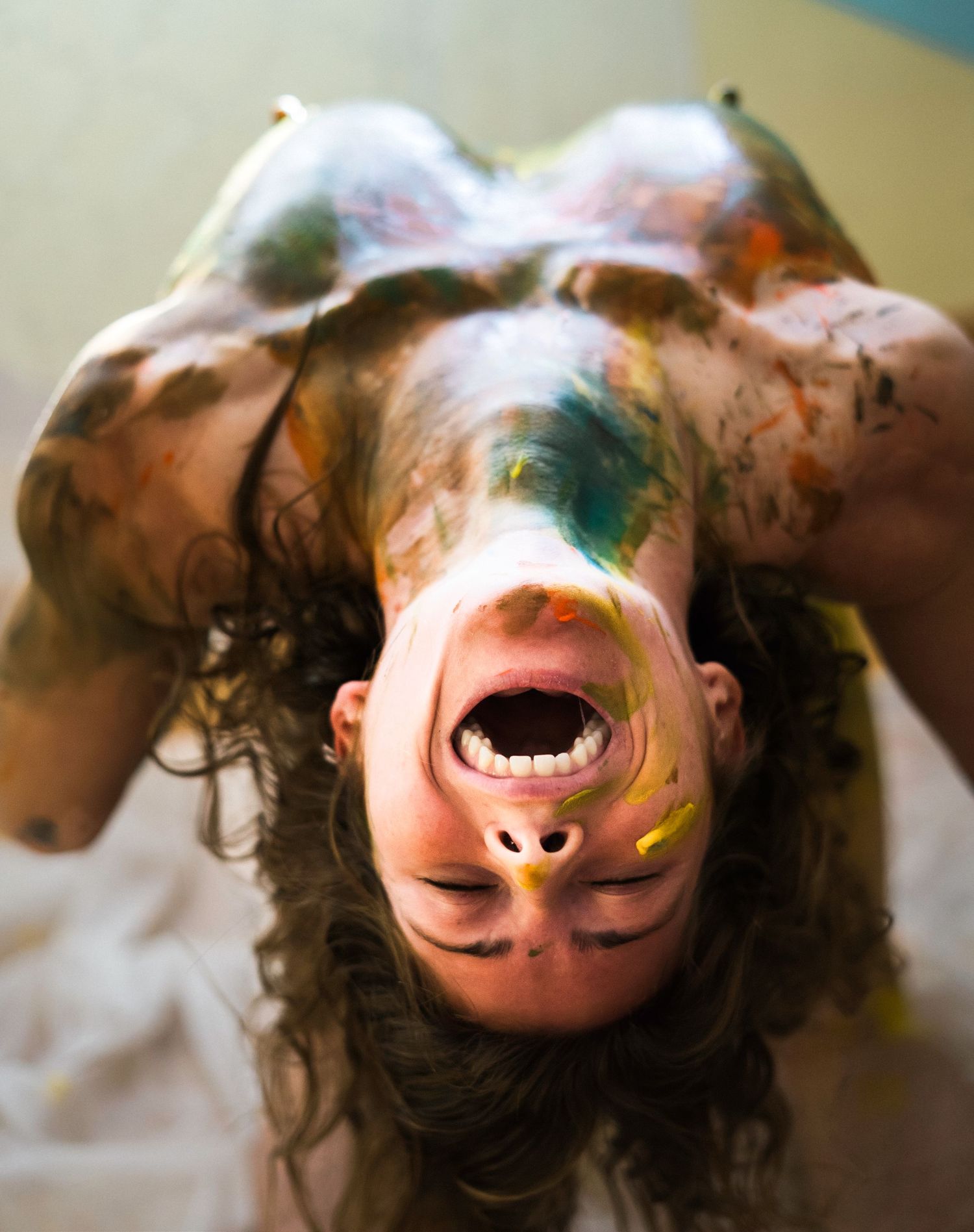 Person with colorful paint on body and face, head tilted back with mouth open, artistic body paint photography.