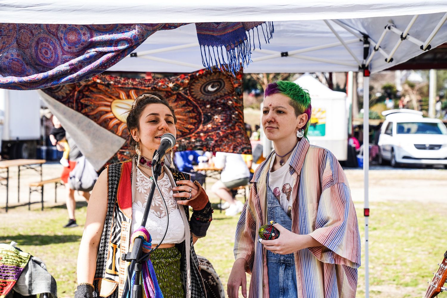 A woman sings while another girl shakes a maraca, both dressed in colorful clothing as they perform a lively street concert in downtown, CO