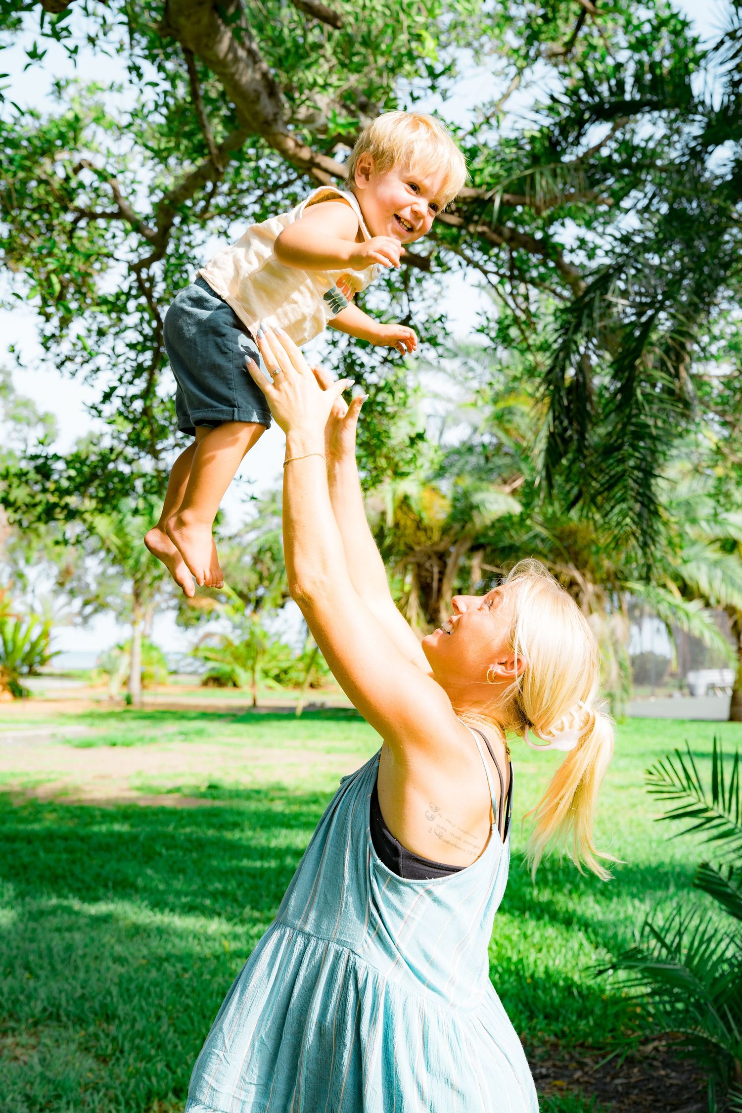 A photo of a pregnant woman throwing her little boy up in the air smiling at the park