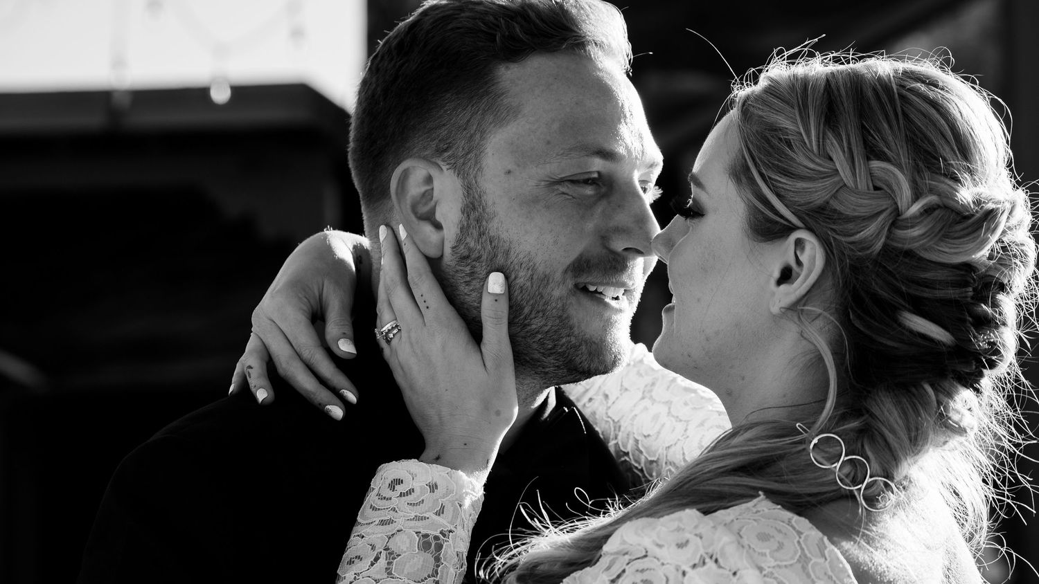Black and white photo of a smiling couple embracing closely on their wedding day, bride in white dress.